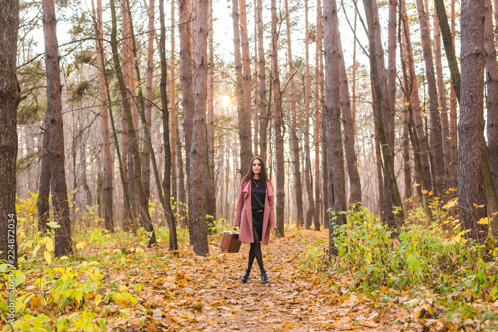 Autumn, season and people concept - woman in pink coat with brown case standing in autumn park over the nature background Autumn, season and people concept - woman in pink coat with brown case standing in autumn park over the nature background