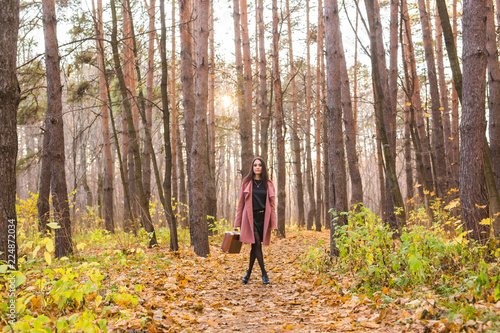 Autumn  season and people concept - woman in pink coat with brown case standing in autumn park over the nature background