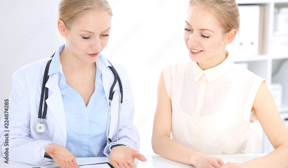 Blonde female doctor and patient talking in hospital office. Health care and client service in medicine Blonde female doctor and patient talking in hospital office. Health care and client service in medicine