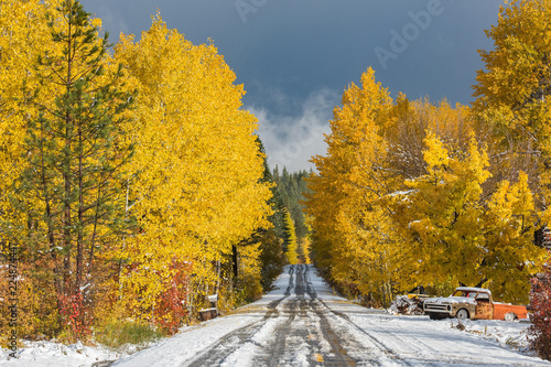 A snow covered road and old truck surrounded by fall color