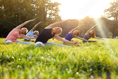 Mixed age group of people practicing yoga outside in the park while sunset