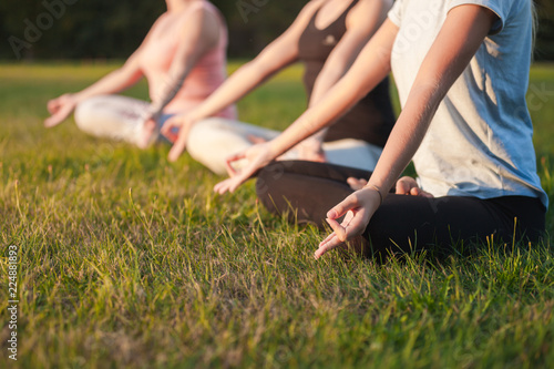Yoga in the park, group of people practicing yoga and meditating while sunset
