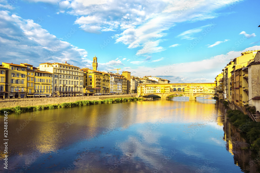 Naklejka premium Panoramic view of the Arno River and stone medieval bridge Ponte Vecchio with beautiful reflection of colorful houses and blue sky with porous clouds, Florence, Tuscany, Italy.