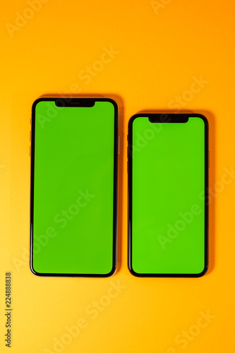 Green chroma key on new mobile smartphne as hero object on bright glamorous modern neon pop orange background - smartphone ready to insert your app photo