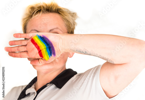 a woman with short blond hair, blurred in a bright background, shows her hand with a painted rainbow photo