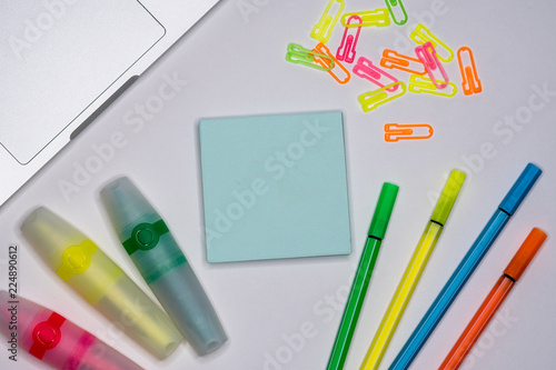 Sticky notes with markers, colored pens, paper clips laying on a table.