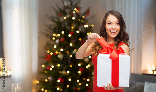 holidays and people concept - smiling woman with gift box over living room and christmas tree background