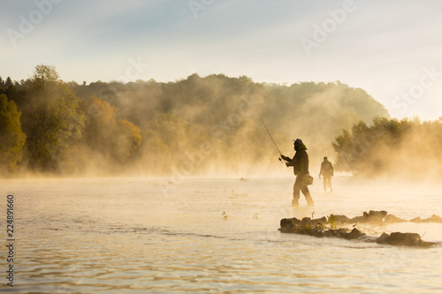 Fishermen holding fishing rod, standing in river