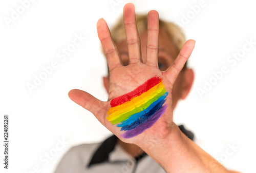 a woman with short blond hair, blurred in a bright background, shows her hand with a painted rainbow photo