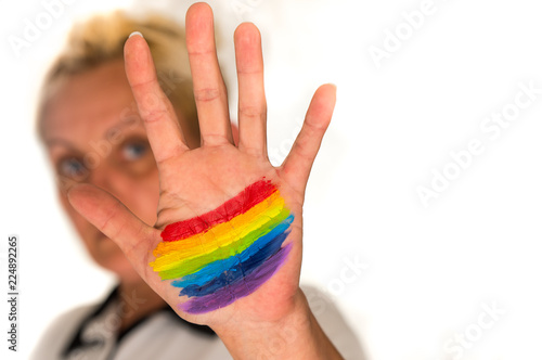 a woman with short blond hair, blurred in a bright background, shows her hand with a painted rainbow