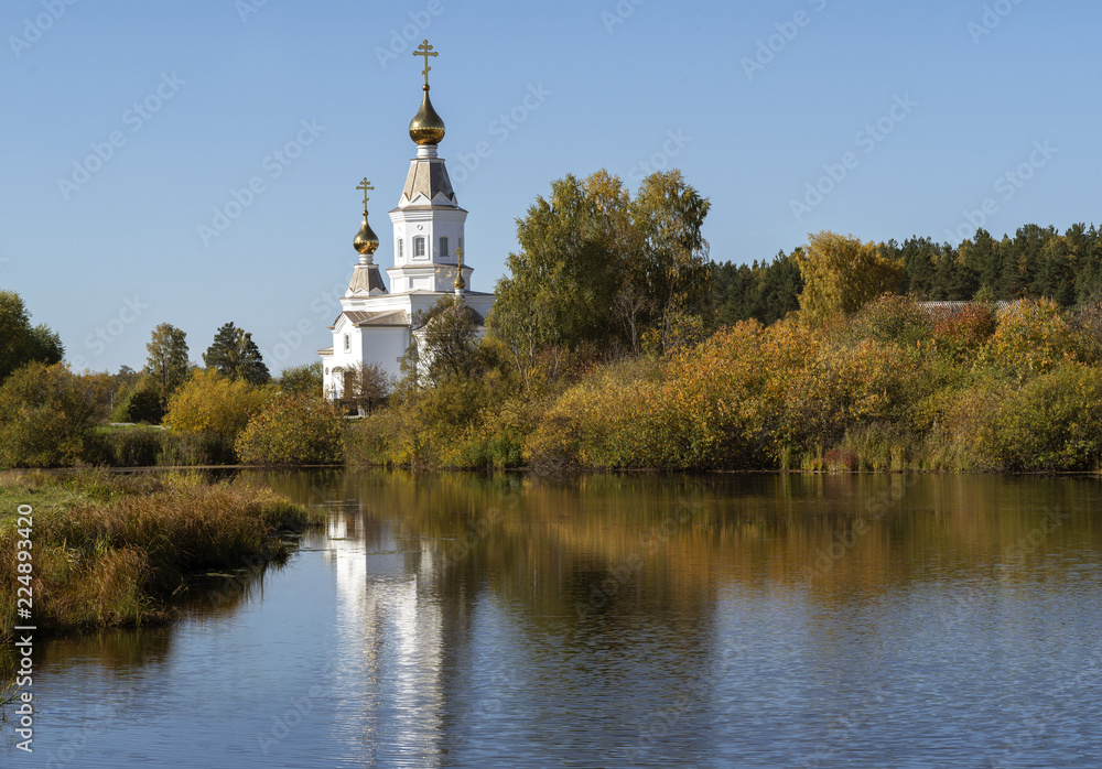 Small orthodox church on a lake shore on a sunny autumn day.