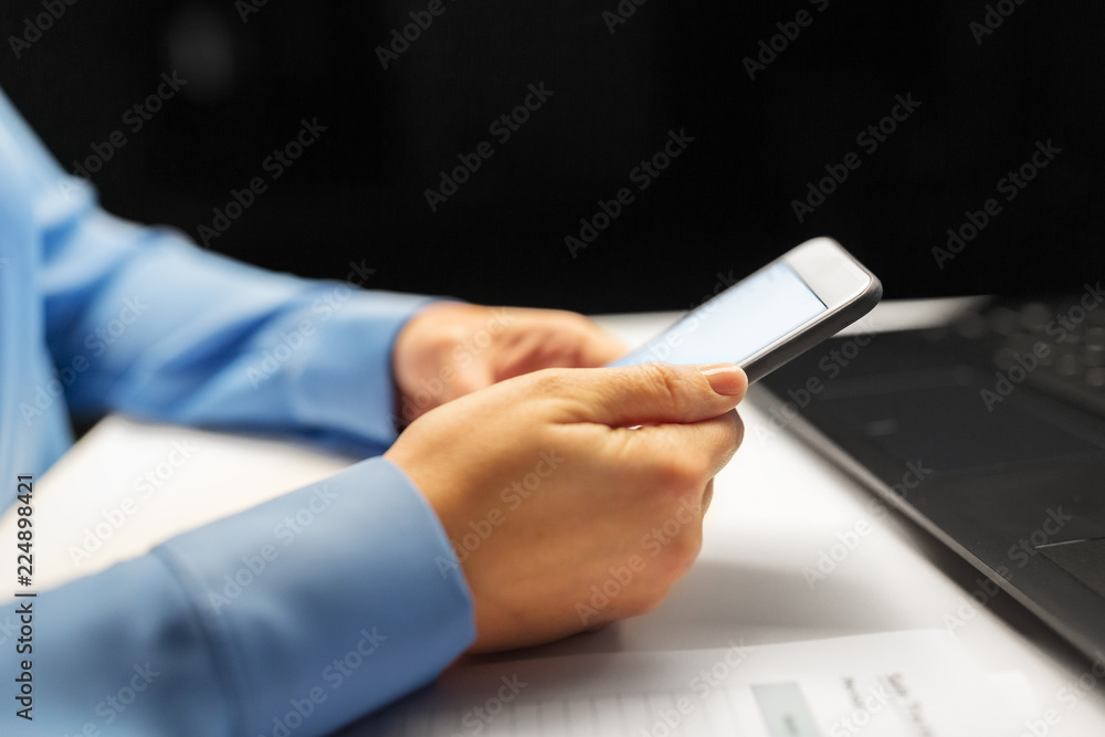 business, deadline and technology concept - close up of businesswoman hands with smartphone and laptop computer working at night office