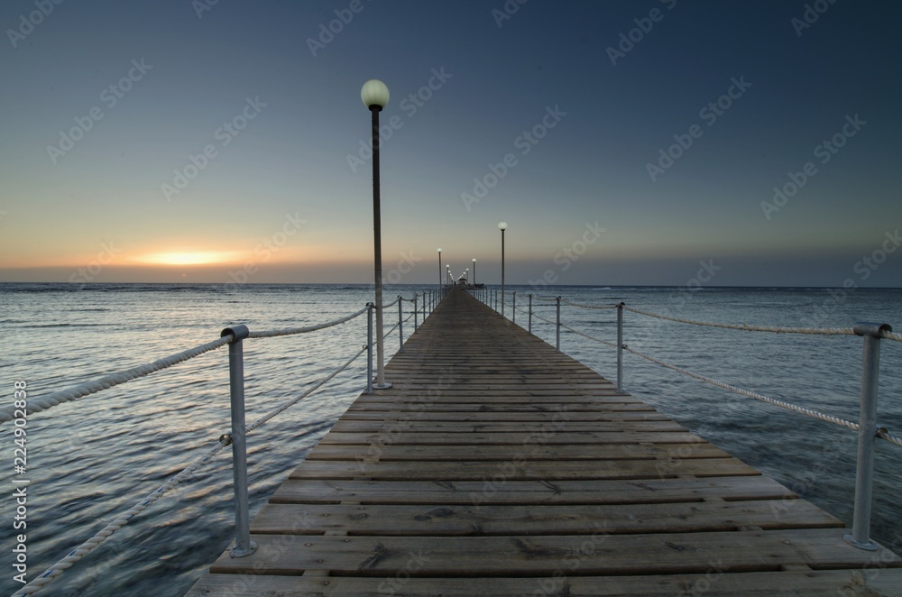Sunrise over the sea and a light wooden pier.