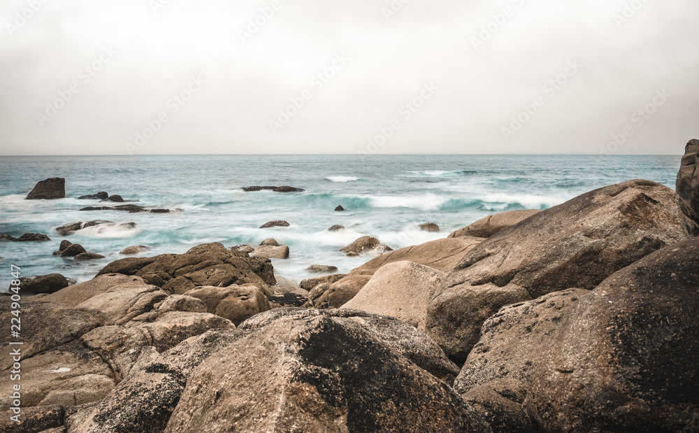 Long exposure of sea on a cloudy day with rocks in foreground, blue yellow contrast