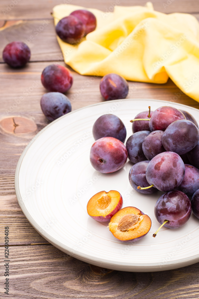 A broken ripe blue plum and whole berries on a plate on a wooden table A broken ripe blue plum and whole berries on a plate on a wooden table