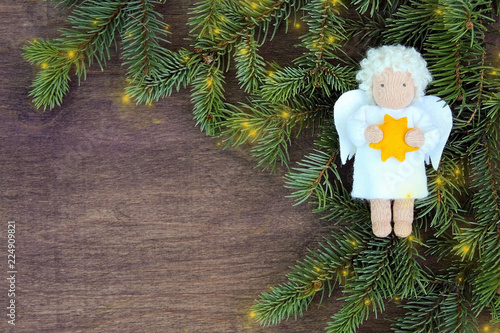 White felt Christmas angel with yellow star in hands to fresh natural branches of Christmas tree spruce on wooden background