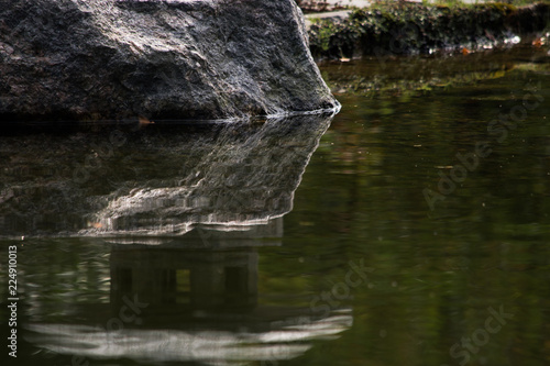 Reflection of a large stone in the surface of the water near the shore