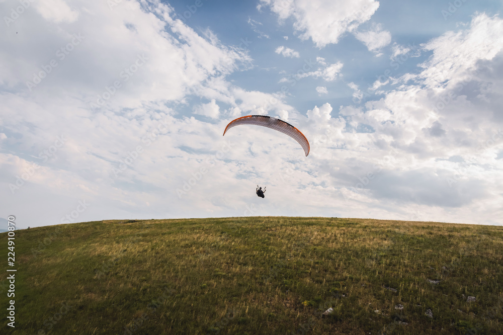 A white-orange paraglider flies over the mountainous terrain