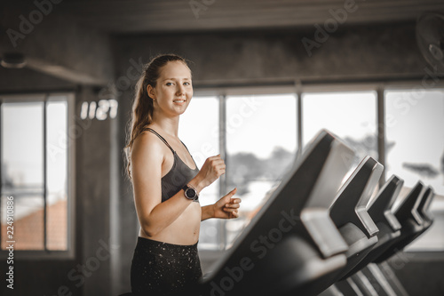Fit young woman caucasian running on machine treadmill workout in gym. Glad smiling girl is enjoy with her training process. Concept of fitness, healthy life, Sport, Lifestyle. Free Download Fit young woman caucasian running on machine treadmill workout in gym. Glad smiling girl is enjoy with her training process. Concept of fitness, healthy life, Sport, Lifestyle. - GFXLoad