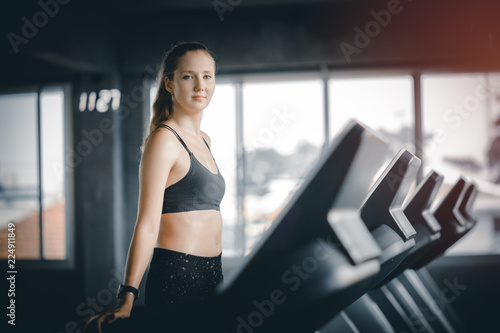 Fit young woman caucasian running on machine treadmill workout in gym. Glad smiling girl is enjoy with her training process. Concept of fitness, healthy life, Sport, Lifestyle.