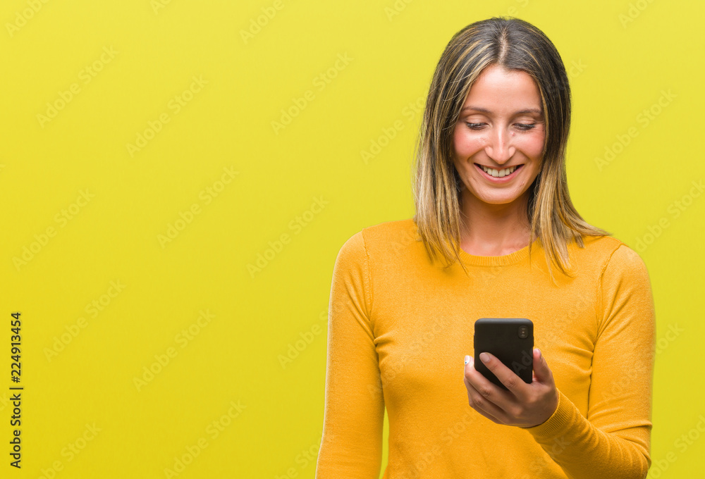 Young beautiful woman sending message using smartphone over isolated background with a happy face standing and smiling with a confident smile showing teeth Young beautiful woman sending message using smartphone over isolated background with a happy face standing and smiling with a confident smile showing teeth