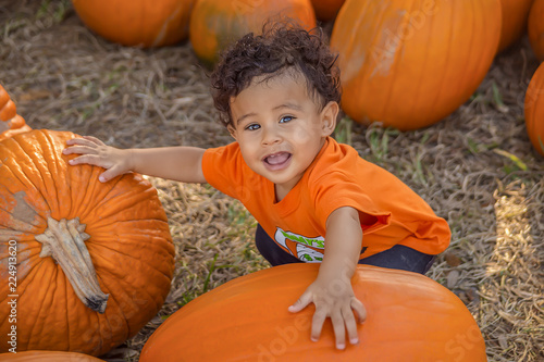 A small boy squats down arms on two pumpkins looking up. photo