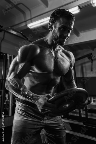 White Muscular man is posing in gym with weight plate and straining muscles BW