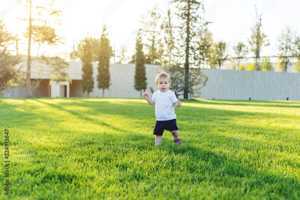 Cute baby runs on a green lawn playing in nature on a Sunny day. Concept one-year-old child and first steps