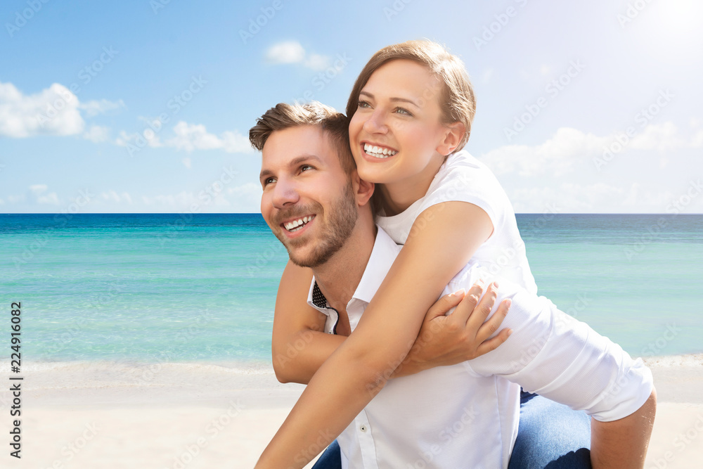 Happy Man Giving Piggyback To His Wife At Beach Happy Man Giving Piggyback To His Wife At Beach