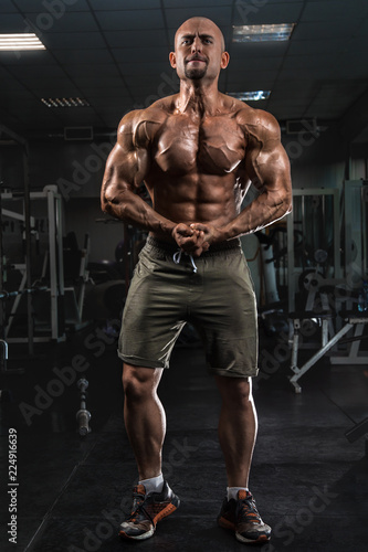 White Muscular man fitness model is posing in the dark gym and straining muscles