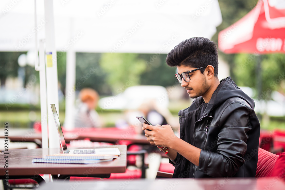 Young indian office worker using his phone in a street cafe - obrazy, fototapety, plakaty 