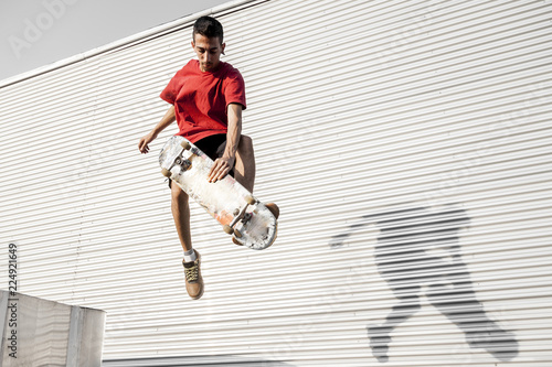 young skateboarder jumps up with his board in front of a metal background