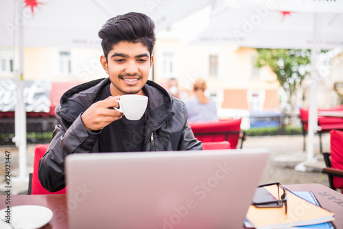 Young indian guy drinking coffee while computing at a student cafe