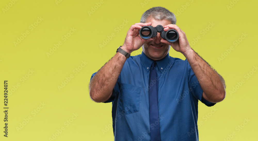 Handsome senior man looking through binoculars over isolated background with a happy face standing and smiling with a confident smile showing teeth Handsome senior man looking through binoculars over isolated background with a happy face standing and smiling with a confident smile showing teeth