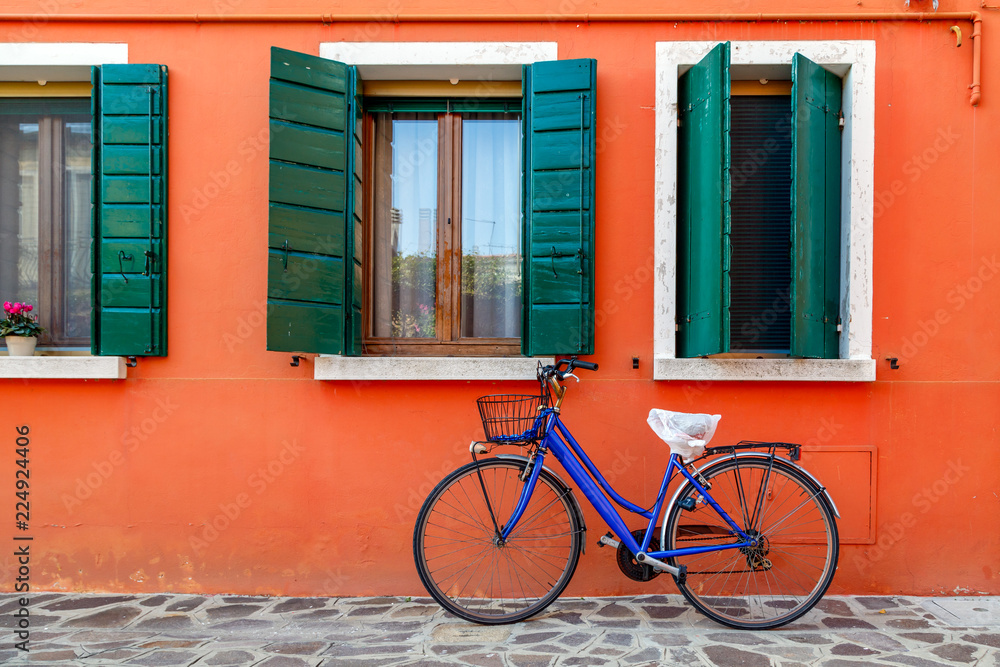 Bicycle with a basket by the wall of colorful house in Burano, Venice, Italy.