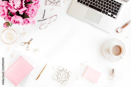 Flat lay women's office desk. Female workspace with laptop, pink peonies bouquet, accessories on white background. Top view feminine background.