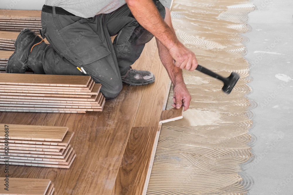 Worker installing wooden flooring boards on applied adhesive - obrazy, fototapety, plakaty 