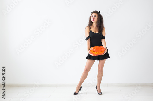 Smiling brunette woman in halloween makeup posing with carved pumpkin over light background with copy space © satura_
