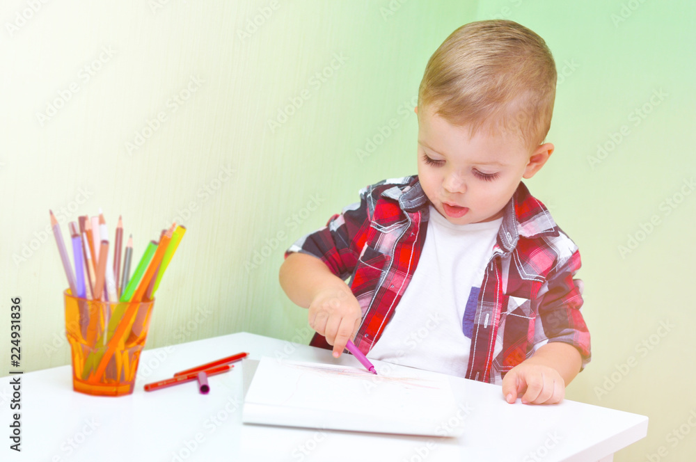 Cute little boy in a red checkered shirt smiles and draws a lilac marker in a white album
Cute little boy in a red checkered shirt smiles and draws a lilac marker in a white album