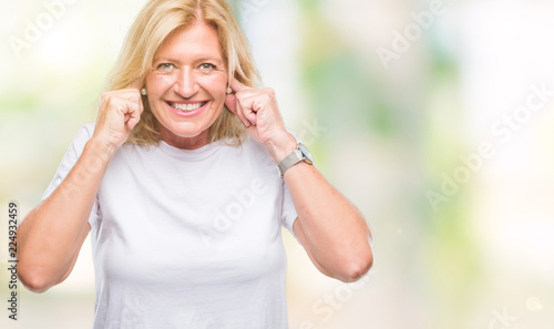 Middle age blonde woman over isolated background covering ears with fingers with annoyed expression for the noise of loud music. Deaf concept.