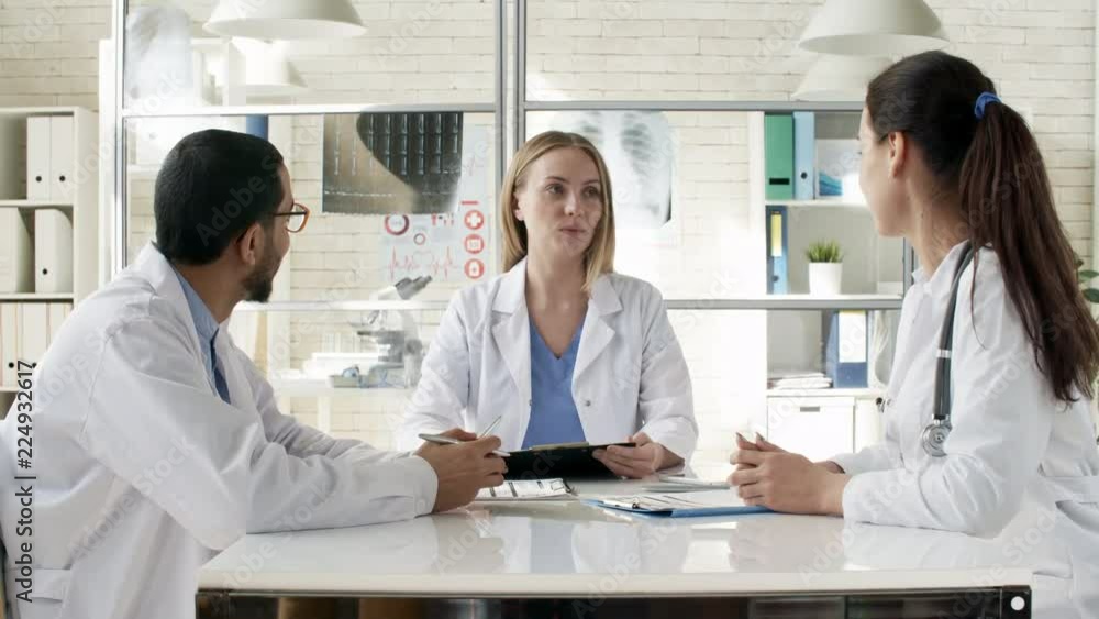 Zoom in shot of young Caucasian woman sitting at desk in medical clinic and talking to multiethnic colleagues during meeting Zoom in shot of young Caucasian woman sitting at desk in medical clinic and talking to multiethnic colleagues during meeting