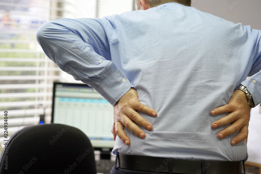 Fototapeta premium Close-up view of a office worker man with pain in kidneys. Young male with back ache clasping her hand to her lower back. Men suffering from ribbing pain, waist pain.