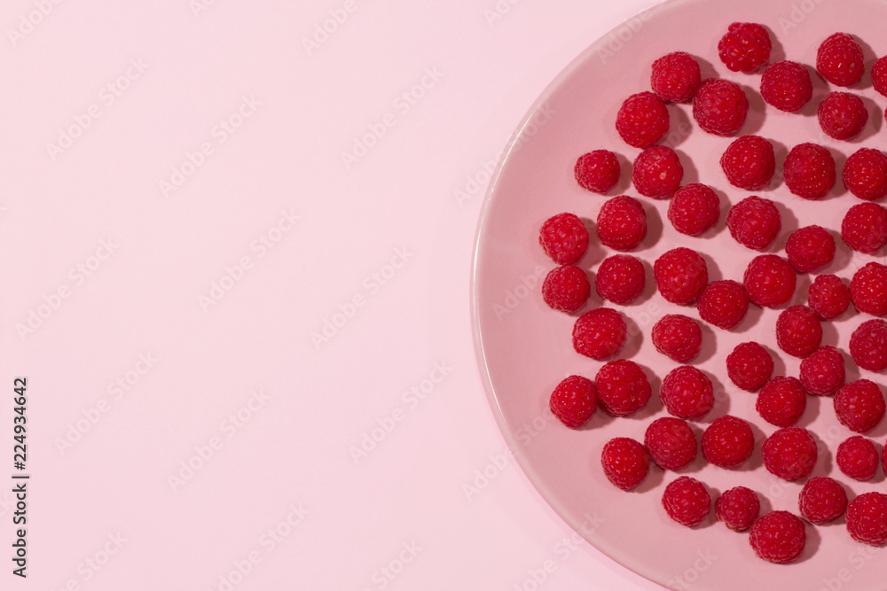 Raspberries on a pastel pink plate on a pastel light blue background. Raspberries on a pastel pink plate on a pastel light blue background.