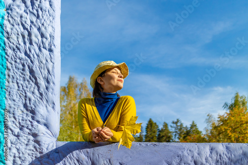 beautiful woman in blue poloneck and yellow cardigan and hat is holding yellow maple leaf photo