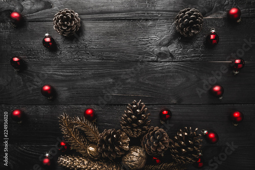 Upper, top, view from above, of evergreen pines, red toys on black wooden background, with space for text writing, greeting.