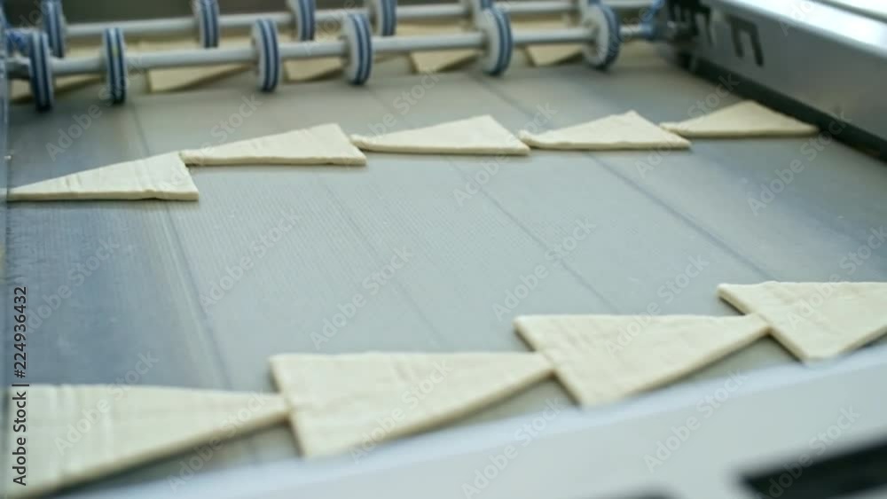 Close up shot of laminated dough for croissants being cut into triangular pieces on conveyor belt at factory Close up shot of laminated dough for croissants being cut into triangular pieces on conveyor belt at factory