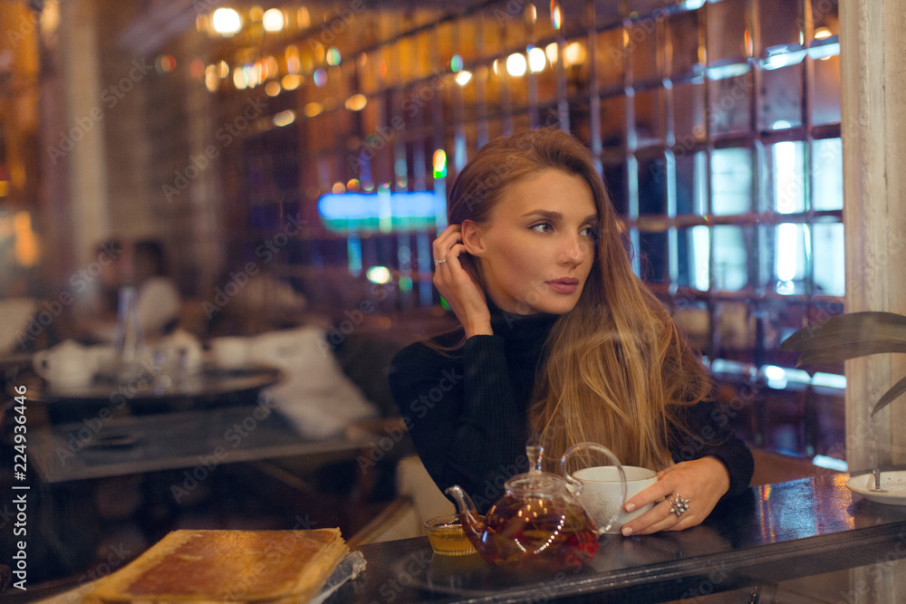 Beautiful evening girl in a cafe drinking tea and looking out the window Beautiful evening girl in a cafe drinking tea and looking out the window