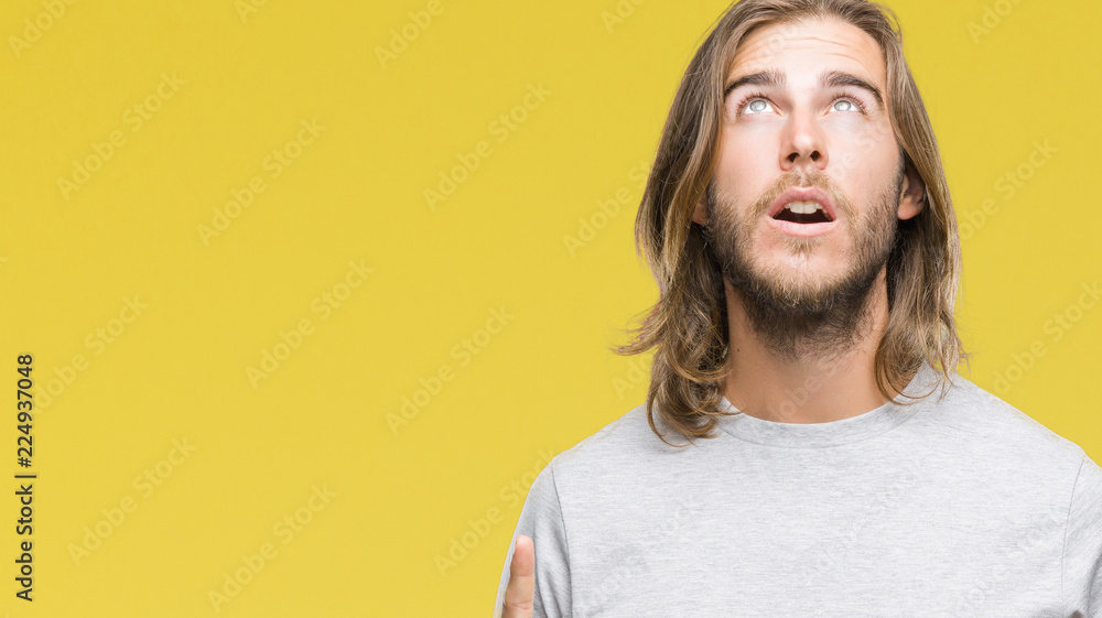 Young handsome man with long hair over isolated background amazed and surprised looking up and pointing with fingers and raised arms. Young handsome man with long hair over isolated background amazed and surprised looking up and pointing with fingers and raised arms.