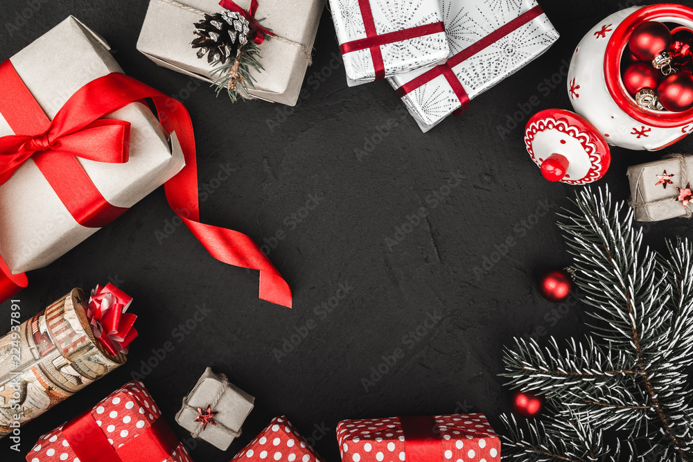 Upper top view of a red ribbon, Christmas presents, tree toys,   and evergreen branch on a stone black background, with space for text writing
