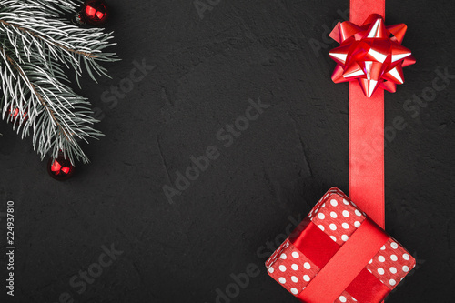 Upper top view of a red ribbon, present and evergreen branch on a stone black background, with space for text writing photo